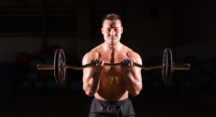 Fototapeta na wymiar Powerful bodybuilder doing the exercises with barbell. Strong male with naked torso on dark background. Strength and motivation.