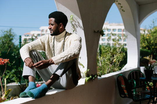 African man seating on balcony, enjoying summer sunny day outdoor at home