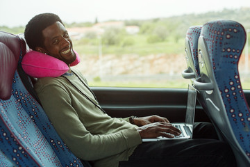 Portrait of smiling man using laptop computer in bus travel - obrazy, fototapety, plakaty