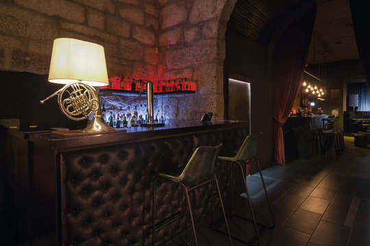 Modern jazz bar interior design, leather bar counter, lamp like music instrument design. Stone wall on background, brutal atmosphere