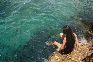 Woman with long hair seating on sea shore and keep legs into water