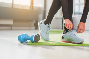 Close up of woman feet and hands. Lady wearing blue sport suit is lacing up right blue sneaker...