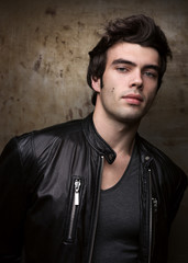 Young man in black leather jacket posing by metal walls. Portrait of the brunette in stylish clothes.