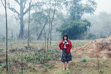 Naklejka premium Young woman wearing red blanket doing pictures on compact camera and walking in fog field morning time