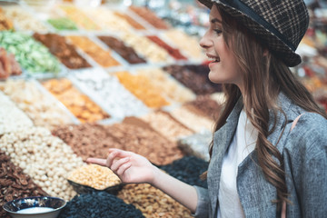 Profile of young woman pointing at variety of seasons and dry fruit. She is smiling in trendy hat while selecting snacks