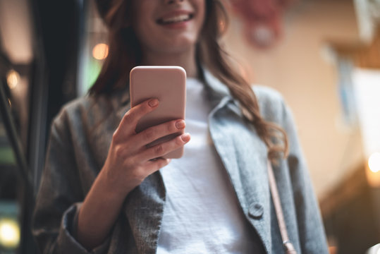 Low angle focus on woman hand holding smartphone. Woman is smiling while communicating via gadget