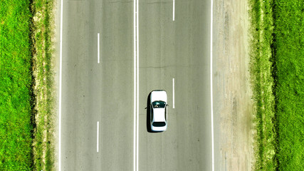 Aerial photo. A white car is driving along the highway parallel to the road markings. Concept of traveling by car.