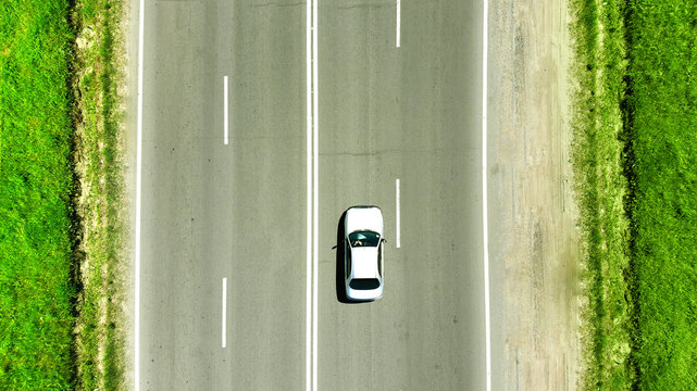 Aerial photo. A white car is driving along the highway parallel to the road markings. Concept of traveling by car.
