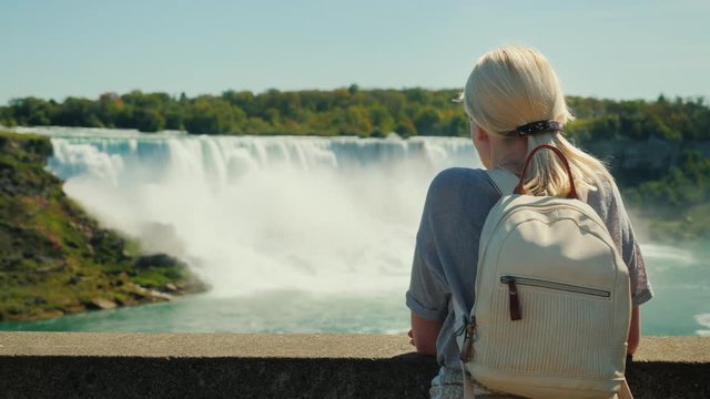 A tourist with a backpack behind him looks at Niagara Falls. Rear view, taken from the Canadian coast. In the picture you can see a waterfall on the American shore