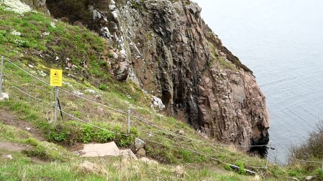 Fenced in steep cliffs in Kullaberg nature reserve, Sweden. A warning sign is posted by the fence. The sea is moving down below.