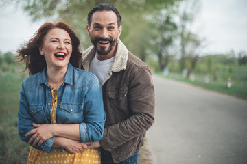 Waist up portrait of carefree mature man and woman having fun in the nature. They are hugging and laughing while standing on the road. Copy space