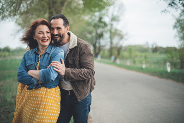Portrait of joyful loving couple are enjoying landscape in countryside. They are standing on alley surrounded by trees and embracing. Copy space 