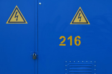 Blue metal doors of outdoor electric cabinet with padlock and two triangle warning signs of...