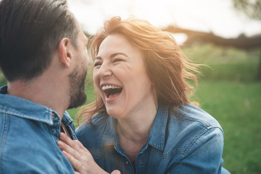 Portrait of excited middle-aged woman is laughing from the joke which man telling her. They are relaxing in the nature and hugging 