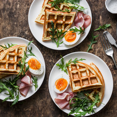 Delicious savory breakfast on a wooden background - boiled eggs, potato waffles and ham, top view