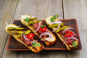 Restaurant meals, gourmet Italian snack, food photo, menu concept. Pickled gherkin and salmon bruschettas on restaurant table