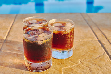 Drinks in glasses by the edge of a swimming pool, a perfect place for summer and everyday.