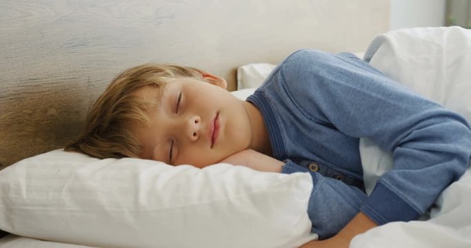 Portrait of the pretty little blonde boy dreaming in a cozy bed in the morning. Indoor