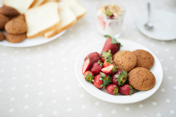 Fresh ripe strawberries and oat cookies in white porcelain bowl on served table