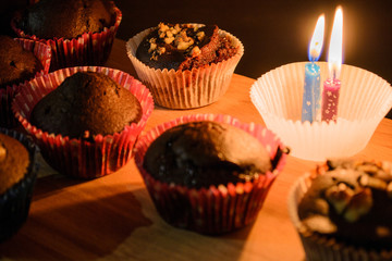 Chocolate muffin on a wooden board next to a burning candle. Warm light. Dessert. Home cosiness. Homemade baking.