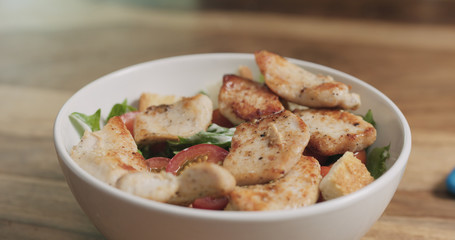 closeup adding chicken to caesar salad