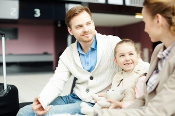 Happy little girl and her parents having talk while waiting for their airplane in airport lounge