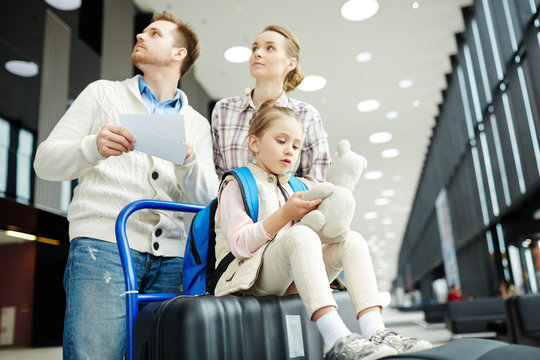 Young couple looking at tableau while moving towards entrance to platform with their daughter sitting on baggage