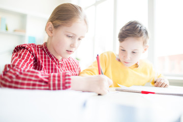 Two schoolkids with highlighters drawing together while carrying out task at lesson