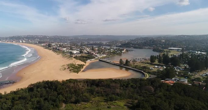 Scenic lagoon of Narrabeen lake at the entrance to Pacific ocean at Narrabeen beach with wide sandy beach and surfing people.
