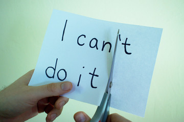 Closeup of hands cutting a piece of paper with "I can't do it" written