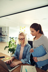 Two businesswomen working together in an office using a laptop