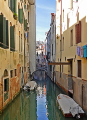 Fototapeta na wymiar View of a typical street in Venice, Italy. Green water canal between houses. Boats at the door