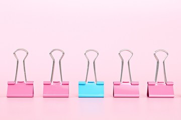 Business, office supplies, leadership, unique, individuality or think different concept : Blue binder clip standing out of pink binder clips on pink background with copy space