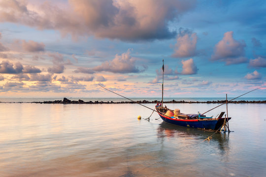 Fishing boat in perfectly calm sea water like glass with the clouds in the sky, long Exposure taken during sunrise
