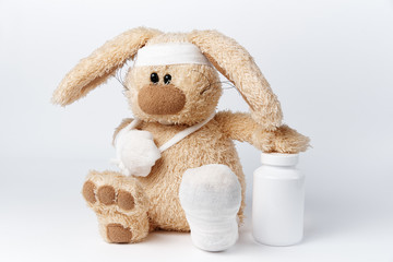 Cute sick bandaged hare with a jar of medicines on a white background.