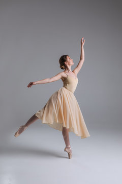 Let yourself become free! Pretty good-looking charming professional ballerina in the beige dress making a pose in a studio.
