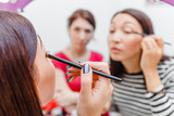 Two young women friends smiling and applying make-up cosmetic at the mirror. Frienship and visage concept
