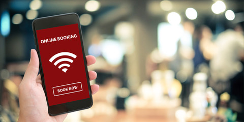 Hand holding smart phone with online booking on screen over blur cafe background, mock up,...