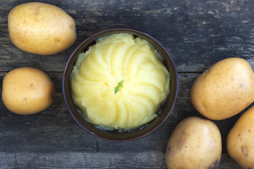 Mashed potatoes and raw potatoes side by side, located on a wooden background, rustic style