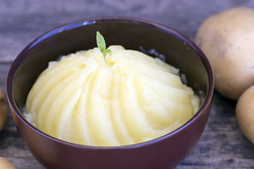 Mashed potatoes and raw potatoes side by side, located on a wooden background, rustic style close-up