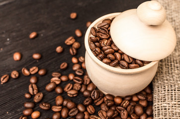 Coffee beans scattered from a wooden pot on black table surface background.