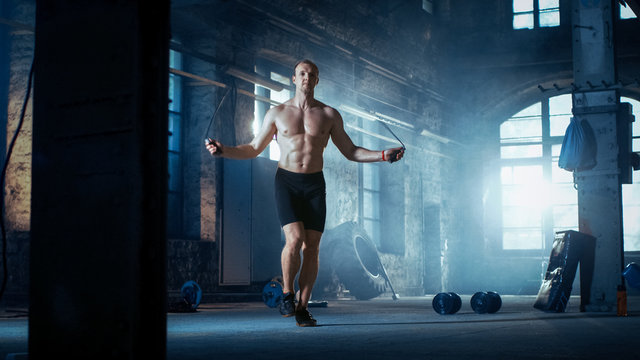 Muscular Fit Man Exercises with Jump / Skipping Rope in a Deserted Factory Hardcore Gym. He's Sweaty from His Cross Fitness Exhausting Training.