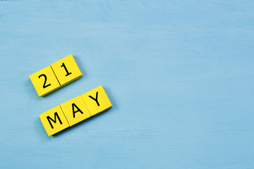 MAY 21, yellow cube calendar on blue wooden surface with copy space