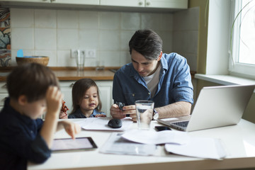 Young father working at home and looking after son and daughter
