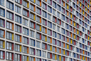 Obraz premium Perspective view of a facade of modern building of concrete with colored inserts on the windows, forming a pattern, as background (abstract)