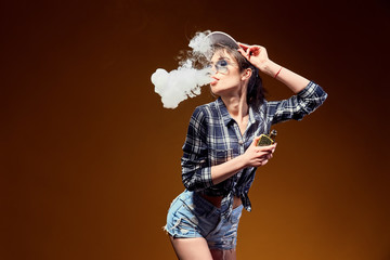 Attractive glamour woman standing and vaping on yellow background.