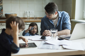 Young father working at home and looking after son and daughter