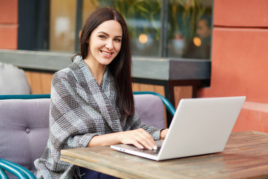 Positive optimstic young female blogger chats online with followers, has happy expression, uses modern laptop computer and free internet in cafe. Pretty student searches information on website