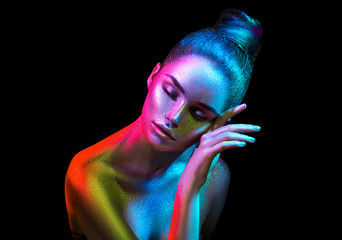 Fashion model woman in colorful bright sparkles and neon lights posing in studio, portrait of...