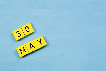 MAY 30, yellow cube calendar on blue wooden surface with copy space